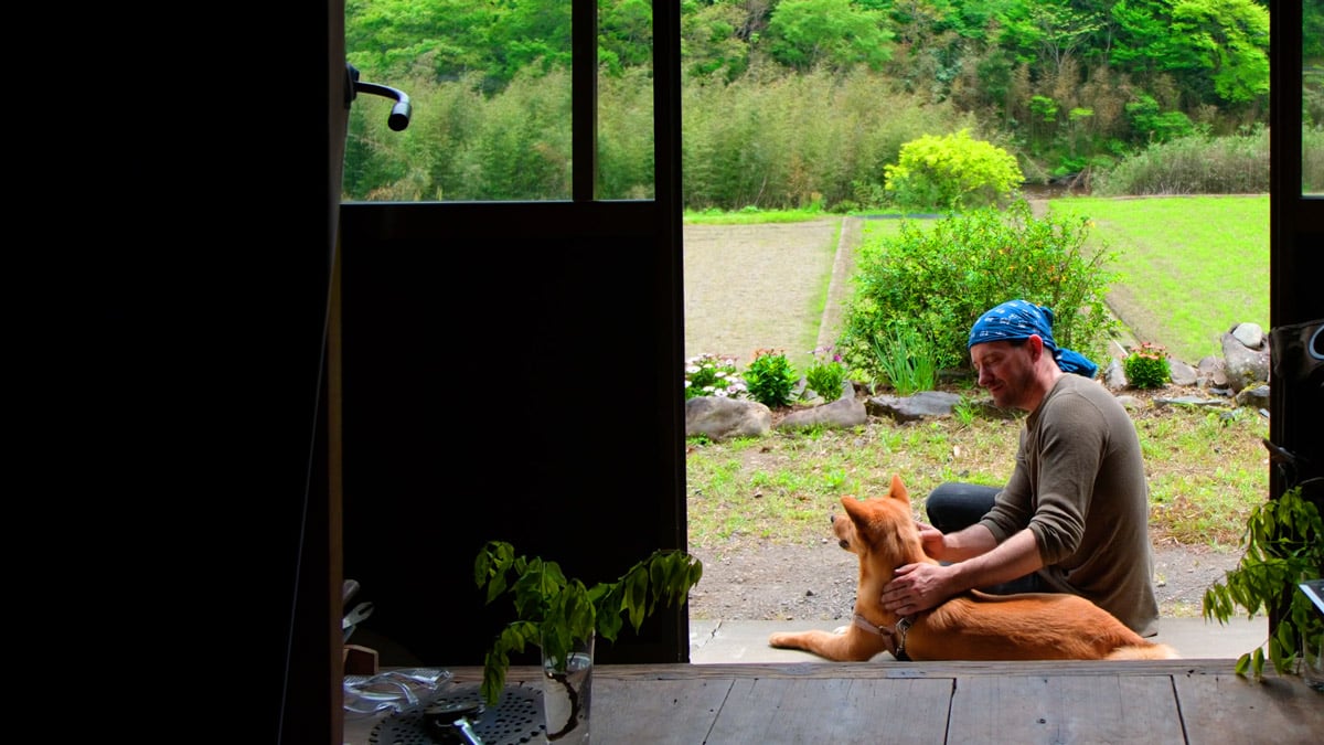 man and dog sitting on ground with greenery in background, framed by open doors